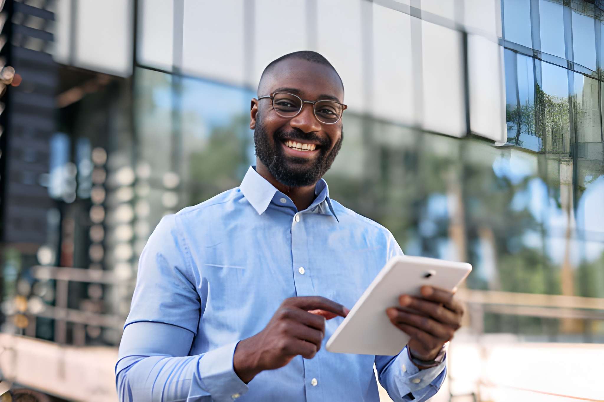 A business owner smiling while working on a tablet outside an office building